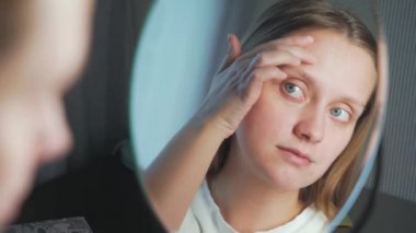 Genç bir kadın aynada kendine bakar, yüzünün derisini inceler ve üzülür. Yüzünde kızarıklık ve sivilceler var. Kız çok üzgün. Sağlık, kozmetoloji