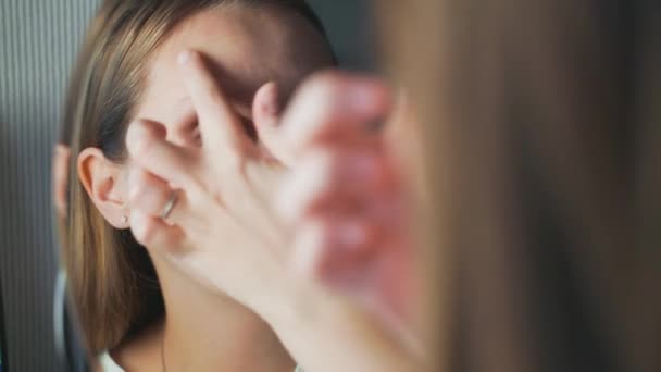 Unge kvinne ser på seg selv i speilet, undersøker huden i ansiktet og blir opprørt. Det er rødhet og kviser i ansiktet. Jenta er opprørt. Helse, kosmetologi – stockvideo