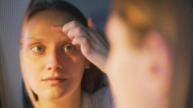 Genç bir kadın aynada kendine bakar, yüzünün derisini inceler ve üzülür. Yüzünde kızarıklık ve sivilceler var. Kız çok üzgün. Sağlık, kozmetoloji