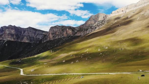 Kuzey Kafkasya 'daki dağ geçidinin hava manzarası. Dağ tepelerinin aralığı parlak güneşi aydınlatır. Yamaçlar yemyeşil ve kayalarla kaplıdır. Bulutların gölgesi çayırlarda koşuyor. — Stok video