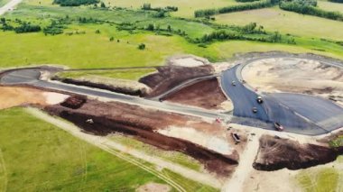 Arabalar için test alanının yol yapımının havadan görüntüsü. Siyah asfalt, kum, ezilmiş taş ve inşaat malzemeli büyük kamyonlar yol boyunca ilerliyor. Yol yapımı, test sahası