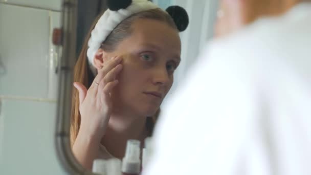 Jeune femme caucasienne se regarde dans le miroir de la salle de bain et examine la peau de son visage et se fâche. Il y a des rougeurs et des boutons sur le visage. La fille est bouleversée. Santé, cosmétologie — Video