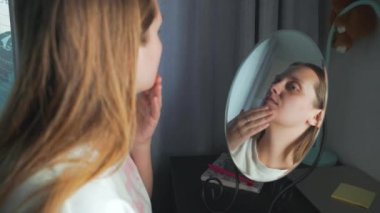 Genç bir kadın aynada kendine bakar, yüzünün derisini inceler ve üzülür. Yüzünde kızarıklık ve sivilceler var. Kız çok üzgün. Sağlık, kozmetoloji