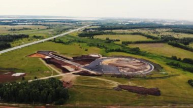 Arabalar için test alanının yol yapımının havadan görüntüsü. Siyah asfalt, kum, ezilmiş taş ve inşaat malzemeli büyük kamyonlar yol boyunca ilerliyor. Yol yapımı, test sahası