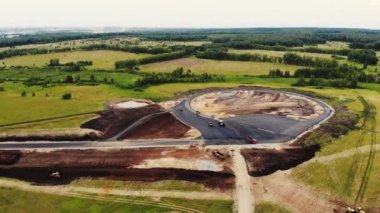 Arabalar için test alanının yol yapımının havadan görüntüsü. Siyah asfalt, kum, ezilmiş taş ve inşaat malzemeli büyük kamyonlar yol boyunca ilerliyor. Yol yapımı, test sahası