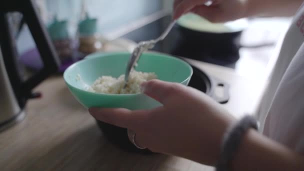 Frau legt frischen gedämpften weißen Reis mit Löffel in tiefblauen Teller. Die Körner des Haferbrei sind bröckelig und werden mit einem kleinen Schieber aufgetragen. Kochen zu Hause, gesunde Ernährung — Stockvideo