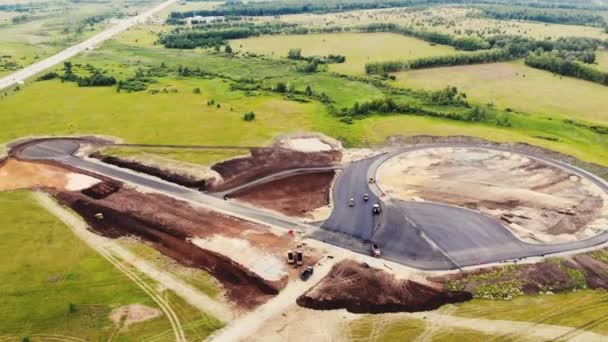 Flygfoto av de gula vägvältarna som lägger asfalten på provningsplatsen för bilar. Bilar rullar smidigt ut svart asfalt längs stigarna. En annan byggutrustning i närheten. Vägbyggnad — Stockvideo