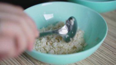 Kadın taze beyaz pirinci kaşıkla koyu mavi tabağa koyar. Yulaf lapası taneleri ufalanır ve küçük slaytlarla uygulanır. Evde yemek yapmak, sağlıklı yemek yemek.