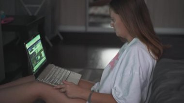 Genç bir kadın TV 'nin karşısında halıda oturuyor ve bulutlu bir sabahta dizüstü bilgisayarla çalışıyor. Kanepeye uzanmış yatıyor. Evde çalışmak, salgın, iş, mesafe