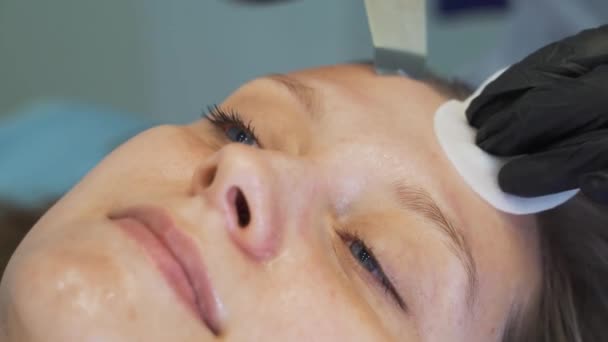 Cosmetologo pulisce la pelle utilizzando un dispositivo di pulizia ad ultrasuoni. Medici mani in guanti stanno facendo scorrere la piastra metallica sul volto dei clienti. Procedura di ringiovanimento, trattamento di acne e brufoli — Video Stock