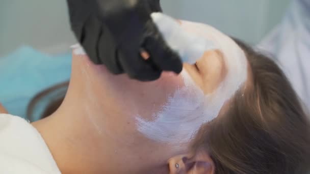 Cosmetologist removes white mask from fair skin of young womans face. Doctor wipes thick white substance from face with white moist sponges. Rejuvenation, white clay, skin cleansing, acne treatment — Stockvideo