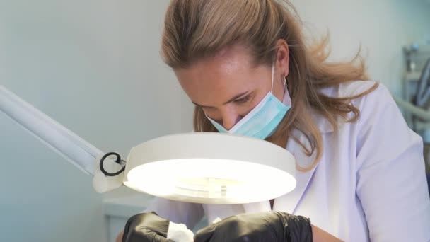 Attractive cosmetologist in coat is working with patient. The doctors hands are in gloves. She carefully looks through magnifying glass at skin and removes dirt. Cosmetology, rejuvenation, skincare — Video Stock
