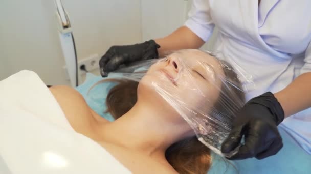 美容師はマスクとラップフィルムを患者の公正な皮膚の上に適用します。若返りの手順,皮膚炎症の治療,にきび治療としわ.現代医学、美容学 — ストック動画