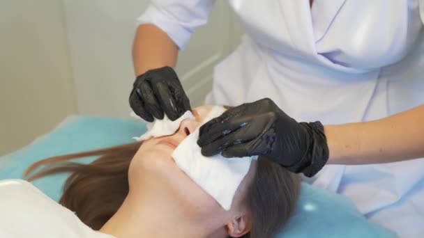 Cosmetoloog veegt jonge vrouwen gezicht met natte witte sponzen van vuil. Ze wrijft zachtjes de patiënten een schone huid om het te reinigen van onzuiverheden. Moderne cosmetologie, acne behandeling, acne, verjonging — Stockvideo