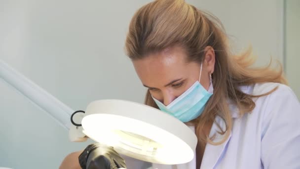 Attractive cosmetologist in coat is working with patient. The doctors hands are in gloves. She carefully looks through magnifying glass at skin and removes dirt. Cosmetology, rejuvenation, skincare — Video Stock