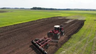 Kırmızı hasat aracı tarlayı geçip toprağı sürüyor. Tarlaya tahıl eker. O araba kullanır ve şerit şeklinde izler bırakır. Rus tarlası, hasat, tahıl, tarım, tarım, tarım, modern teknolojiler