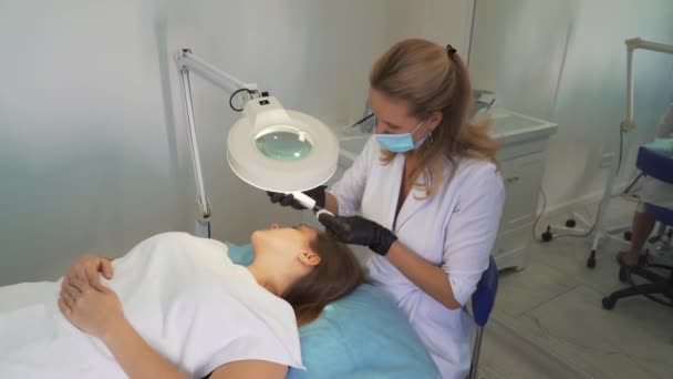 Kozmetik uzmanı deriyi ultrasonik temizlik cihazıyla temizliyor. Eldivenli doktorlar müşterinin yüzünü metal plakayla kaplıyor. Yenilenme prosedürü, sivilce ve sivilce tedavisi — Stok video