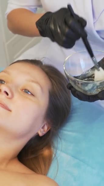 Cosmetologue applique masque sur la peau des femmes visage à des fins thérapeutiques. Patient est couché sur le canapé et la substance transparente épaisse est appliquée sur le visage avec une brosse. Rajeunissement, traitement de l'acné — Video