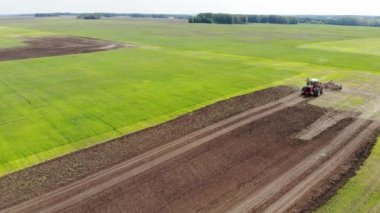 Kırmızı hasat aracı tarlayı geçip toprağı sürüyor. Tarlaya tahıl eker. O araba kullanır ve şerit şeklinde izler bırakır. Rus tarlası, hasat, tahıl, tarım, tarım, tarım, modern teknolojiler