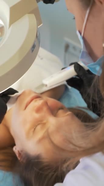 Kozmetik uzmanı deriyi ultrasonik temizlik cihazıyla temizliyor. Eldivenli doktorlar müşterinin yüzünü metal plakayla kaplıyor. Yenilenme prosedürü, sivilce ve sivilce tedavisi — Stok video