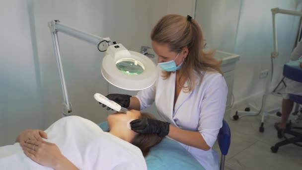 Cosmetologist cleans skin using ultrasonic cleaning device. Doctors hands in gloves are running metal plate over the clients face. Rejuvenation procedure,treatment of acne and pimples — 图库视频影像