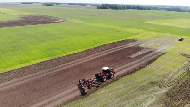 Red harvester drives across field and plows earth. Sows grain in field. He drives and leaves tracks in form of stripes. Russian field, harvesting, grain, agriculture, cultivation, modern technologies — Vídeo de stock