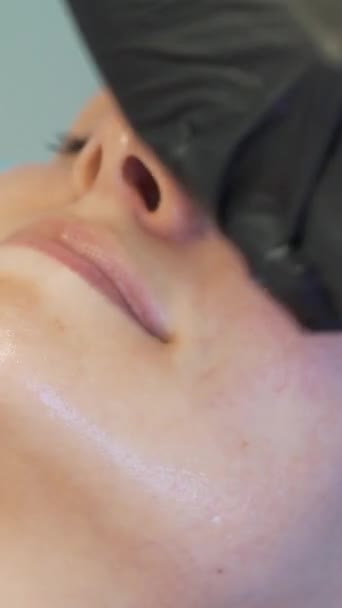 美容师为治疗目的将面罩涂在女性面部皮肤上。病人躺在沙发上，用厚厚的透明物质刷着脸。康复、痤疮治疗 — 图库视频影像