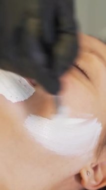 Kozmetik uzmanı kadın derisine tedavi amaçlı maske takıyor. Hasta kanepede yatıyor ve kalın beyaz madde fırçayla yüzüne uygulanıyor. Gençleştirme, sivilce tedavisi