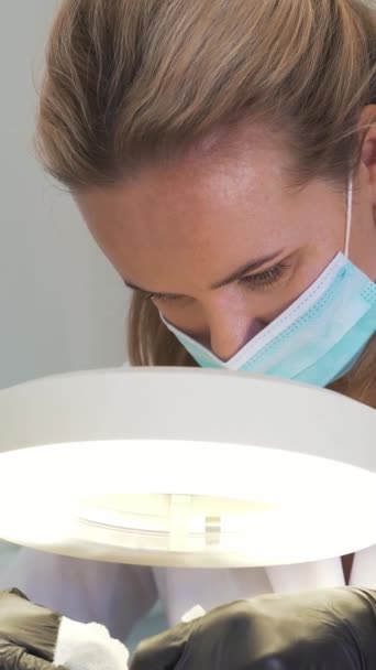 Aantrekkelijke cosmetoloog in vacht werkt samen met patiënt. De dokters hebben handschoenen aan. Ze kijkt zorgvuldig door vergrootglas naar de huid en verwijdert vuil. Cosmetologie, verjonging, huidverzorging — Stockvideo