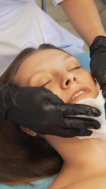 Kozmetik uzmanı genç bir kadının yüzünü ve boynunu ıslak beyaz süngerlerle siliyor. Hastaları safsızlıklarından arındırmak için cildini nazikçe ovuyor. Kozmetik, akne tedavisi, sivilce, gençleştirme — Stok video