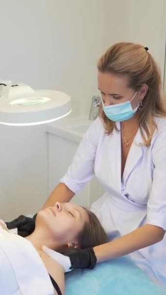 Cosmetologist wipes neck and chest of young woman from dirt with wet white sponges. She gently rubs the patients fair skin to clean it of impurities. Cosmetology, acne treatment, acne, rejuvenation — Stockvideo