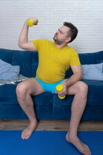 Komik şişman adam aktif olarak sarı küçük dambıllarla spor yapıyor. Sporcu aktif olarak bisepsler ve gülümsemeler için egzersiz yapar. Neşeli, kendini beğenmişlik. Kilo kaybı, spor, kendini soyutlama
