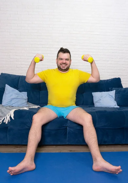 Komik şişman adam aktif olarak sarı küçük dambıllarla spor yapıyor. Sporcu aktif olarak bisepsler ve gülümsemeler için egzersiz yapar. Neşeli, kendini beğenmişlik. Kilo kaybı, spor, kendini soyutlama