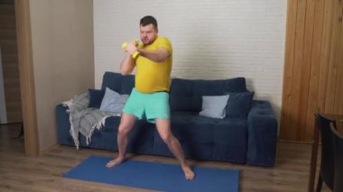 Komik şişman adam aktif olarak sarı küçük dambıllarla spor yapıyor. Sporcu aktif olarak bisepsler ve gülümsemeler için egzersiz yapar. Neşeli, kendini beğenmişlik. Kilo kaybı, spor, kendini soyutlama