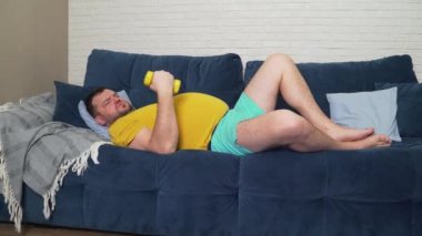 Komik şişman adam aktif olarak sarı küçük dambıllarla spor yapıyor. Sporcu aktif olarak bisepsler ve gülümsemeler için egzersiz yapar. Neşeli, kendini beğenmişlik. Kilo kaybı, spor, kendini soyutlama