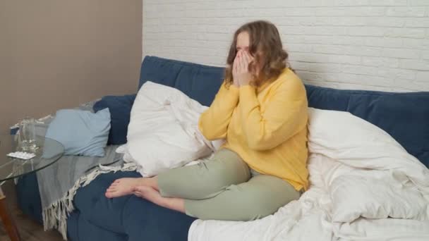 Žena ve svetru sedí na posteli, kašle a kýchá. Má rýmu, chřipku, koronavirus. Bolí ji v krku. Má horečku a zabalí se do přikrývky. Chřipka, nachlazení, izolace epidemie koronaviru — Stock video