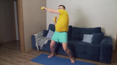 Komik şişman adam aktif olarak sarı küçük dambıllarla spor yapıyor. Sporcu aktif olarak bisepsler ve gülümsemeler için egzersiz yapar. Neşeli, kendini beğenmişlik. Kilo kaybı, spor, kendini soyutlama