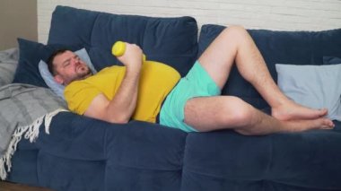 Komik şişman adam aktif olarak sarı küçük dambıllarla spor yapıyor. Sporcu aktif olarak bisepsler ve gülümsemeler için egzersiz yapar. Neşeli, kendini beğenmişlik. Kilo kaybı, spor, kendini soyutlama