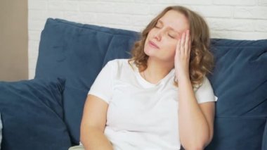 Genç kadının başı ağrıyor, migreni var ve elleriyle baş şakaklarına masaj yapıyor. Bardak alır ve su içer. Derin nefes alıyor. Soğuk algınlığı, grip, migren, salgın, kramp