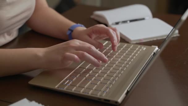 Vrouwelijke handen typen tekst op laptop toetsenbord. Vingers drukken snel op de toetsen op het toetsenbord. Er staat een notitieboekje naast. Persoonlijke computer, thuiswerken, zaken doen, studeren, berichten sturen, chatten — Stockvideo