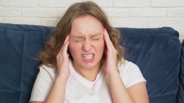 Ung kvinna masserar aktivt tinningarna i huvudet på grund av huvudvärk, migrän, kramper. Det finns lidande, smärta, förtvivlan i hennes ansikte, hon andas djupt. förkylning, influensa, migrän, epidemi, kramper — Stockvideo