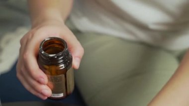 Beyaz yuvarlak tabletler açık bir cam şişeden titreyen elin üzerine dökülüyor. Hap yığını. İntihar, aşırı doz. Beslenme takviyeleri, vitaminler, grip tedavisi, nezle, depresyon, koronavirüs