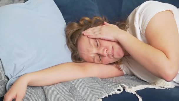 La jeune femme s'allonge sur le lit les yeux fermés et masse les tempes de la tête en raison de migraines. Elle a mal à la tête. Elle souffre et souffre au visage. Rhume, grippe, migraine, épidémie, crampes — Video