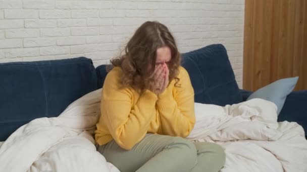 Женщина в свитере сидит на кровати и кашляет и чихает. У нее простуда, грипп, коронавирус. Горло болит. У неё лихорадка и она завернута в одеяло. Эпидемия гриппа, холода, коронавируса — стоковое видео