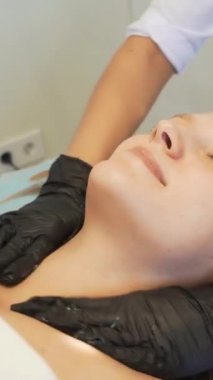 Kozmetik uzmanı, kadınların boyun ve göğüs açık tenlerine dairesel hareketlerle besleyici krem uyguluyor. Deriyi kirlilikten arındırıyor. Doktor randevusu. Deri temizleme, gençleştirme, sivilce tedavisi