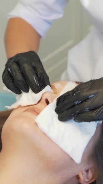 Cosmetologue essuie les jeunes femmes visage avec des éponges blanches humides de la saleté. Elle frotte doucement la peau claire des patients pour la nettoyer des impuretés. Cosmétologie moderne, traitement de l'acné, acné, rajeunissement — Video