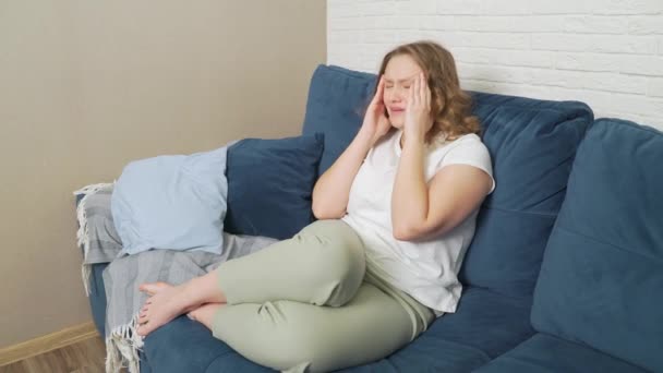 La jeune femme est assise sur le lit, elle a des migraines. Elle masse les tempes de sa tête à cause de graves spasmes. Souffrant au visage, elle respire profondément. Rhume, grippe, migraine, épidémie, crampes — Video