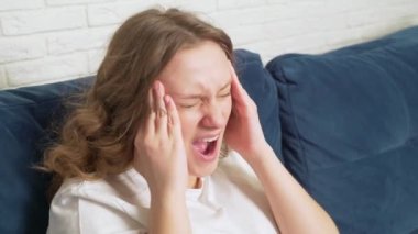 Genç bir kadın baş ağrısı, migren ve spazmlar nedeniyle şakaklarına masaj yapıyor. Yüzünde ıstırap, acı, umutsuzluk var, derin derin nefes alıyor. Soğuk algınlığı, grip, migren, salgın, kramp