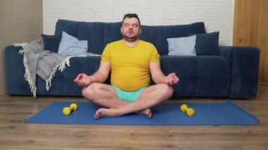 Sarı tişörtlü adam lotus pozisyonunda mindere oturmuş meditasyon yapıyor. Yoga yapıyor. Yavaşça ve eşit bir şekilde nefes alıp ver. İyileşme, rahatlama, farkındalık, meditasyon, yoga