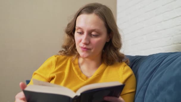 Femme lit un livre de papier relié. Elle feuillette les pages et passe ses yeux au-dessus des lignes du livre. Surprise par ce qu'elle a lu. Lecture fascinante, loisirs, développement personnel — Video